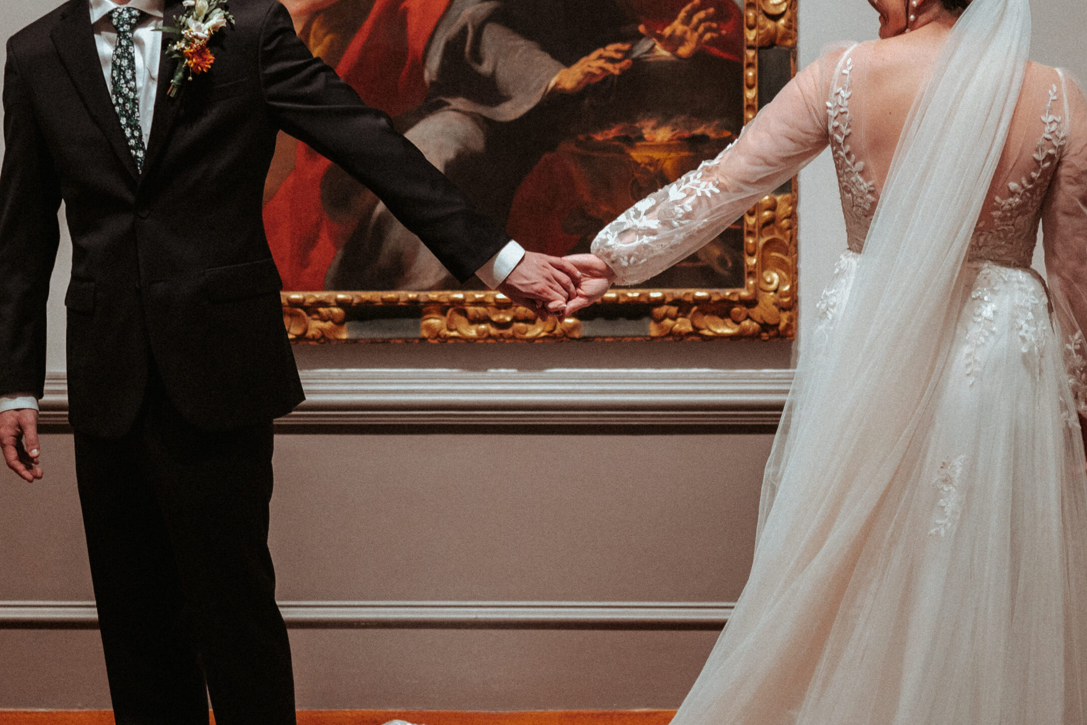 Married couple holding hands in a gallery in front of an artwork.