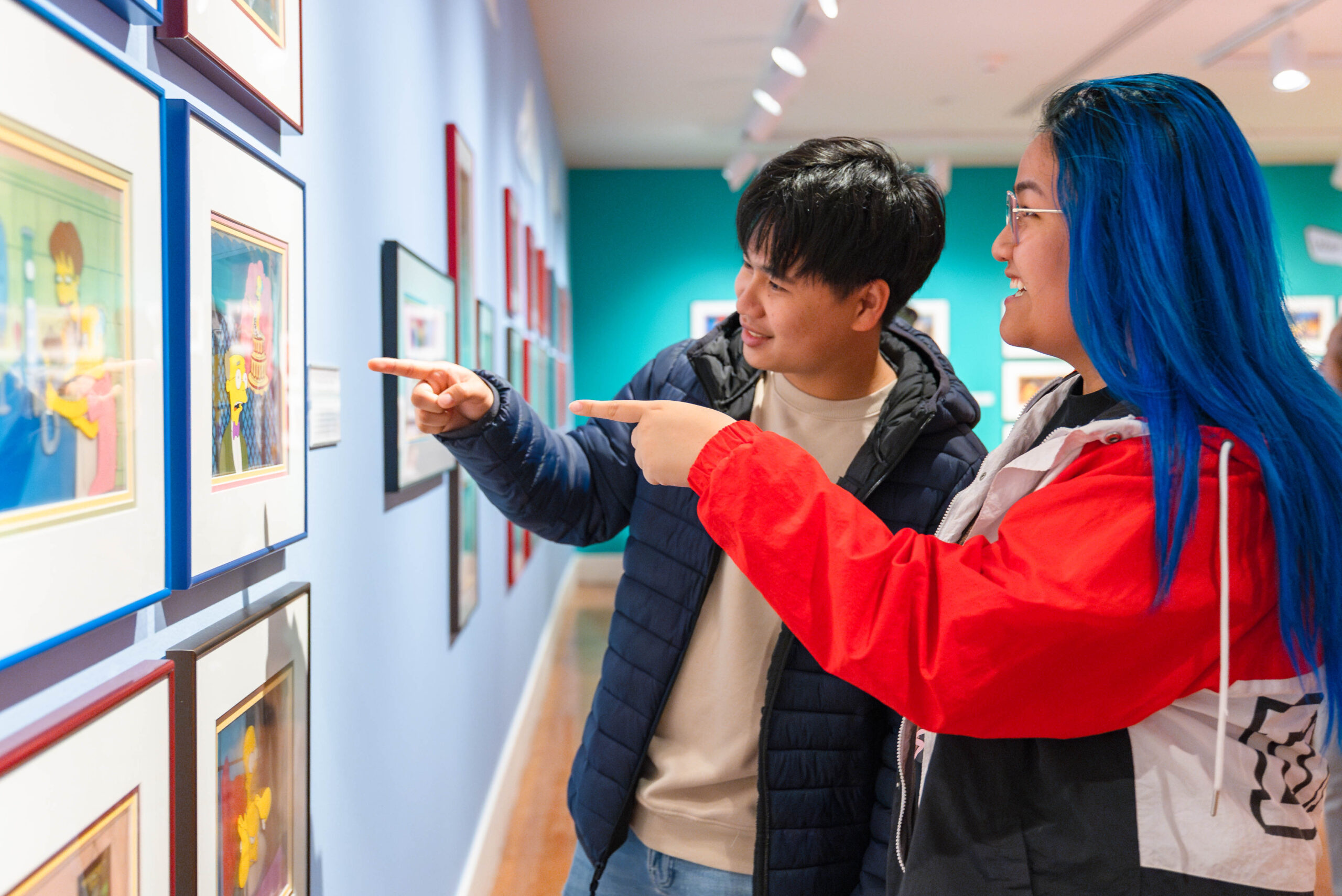 Two visitors gesture toward a wall with artwork.